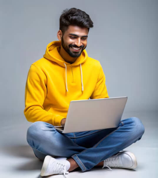 Smiling young man in a yellow hoodie using a laptop