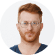 Serious man with red hair and glasses against a plain background